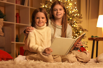 Poster - Cute happy little girls with book reading Christmas story at night