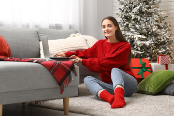 Poster - Young woman in sweater using laptop at home on Christmas eve