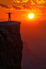 Wall Mural - Silhouette of a Person Standing on a Cliff Edge at Sunset with Vibrant Orange Sky and Sun in the Background