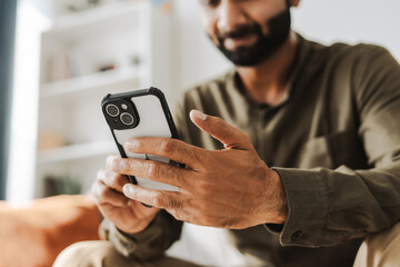 young man smiling while holding mobile phone, using mobile app at home, selective focus on hand