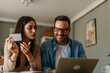 © La Famiglia - Young cheerful couple shopping online at home. Couple shopping online with credit card and laptop.
