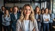 © TENGKUIZAHAM - Confident businesswoman smiling with arms crossed in front of business team