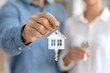 © Downloads - Smiling couple holding keys in front of a new home representing real estate first time buyers and life milestones