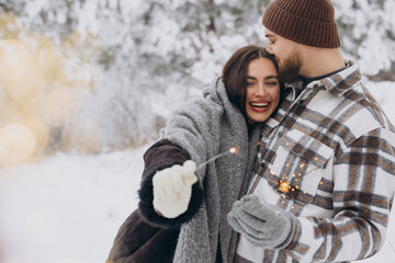 Wall Mural - Happy romantic couple in love holding sparklers in snowy winter forest