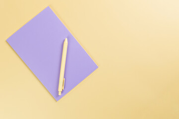 Wall Mural - Top view of purple notebook, yellow pen on yellow background. School, office wallpaper. Flat lay, copy space.