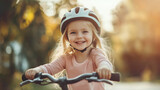 Mała dziewczynka w niebieskim kasku z uśmiechem od ucha do ucha eksploruje okoliczne alejki na swoim rowerze.