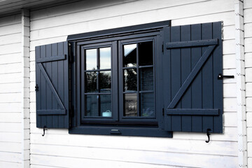 Elegant wooden window with dark shutters on a white house during daylight