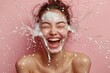 © radekcho - Pretty woman laughing while getting splashed in the face with milk. Female with skin cream splash on pastel background. Aesthetic model with splash, skin care for sustainable facial health, wellness.