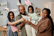 © Seventyfour - Family posing together while celebrating Easter, wearing bunny ears, and holding Easter crafts and decorations indoors