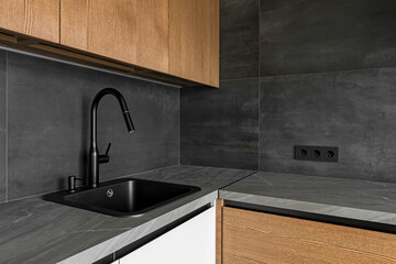 Dark grey kitchen table top, sink with water tap, against a dark grey tiled wall