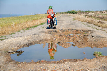 Woman riding alone on a bicycle on broken and pot-holed roads discovering natural environments. 