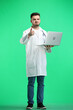 © Katsiaryna - The doctor, in full height, on a green background, uses a laptop