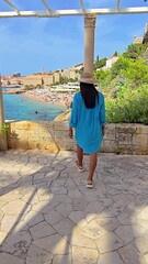 Wall Mural - a woman dressed in an elegant turquoise dress saunters gracefully towards the picturesque harbor of 
