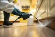 © Yuliia - close-up photo of a pest control worker's hand spraying pesticide on a wooden cabinet in a kitchen.
