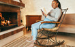 © DisobeyArt - African woman reading book in front of cozy fireplace at home - Autumn and winter lifestyle concept - Focus on face