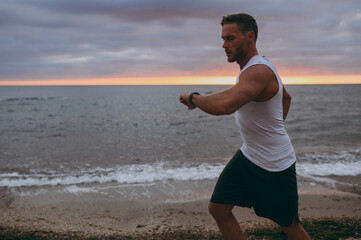 Wall Mural - Side view young strong sporty athletic toned fit sportsman man wear sports clothes look at hand smart watch warm up train at sunrise sun dawn over sea beach outdoor on seaside in summer day morning