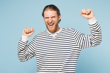 Poster - Young happy man he wear striped sweatshirt casual clothes doing winner gesture celebrate clenching fists dancing isolated on plain pastel light blue cyan background studio portrait. Lifestyle concept.