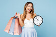 © ViDi Studio - Young fun woman wear casual clothes hold in hand paper package bags after shopping show clock time look camera isolated on plain light pastel blue cyan background. Black Friday sale buy day concept.