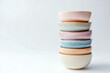 © tynza - Handmade ceramic bowls stacked on top of each other in various pastel colors, set against a white background.