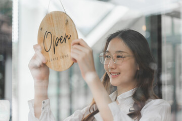 Young female shop owner holding the Open sign that hanging on the shop glass window