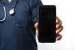 © ArvStd - Smiling young Asian man nurse working wearing a blue uniform showing smartphone with blank screen isolated on white background. Healthcare medicine concept