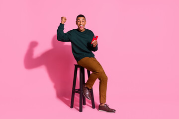 Poster - Full length photo of loucky positive guy dressed pullover sitting bar chair winning game modern gadget emtpy space isolated pink color background