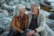 © Nico - Joyful Older Couple Sitting on Rocks by the Shore