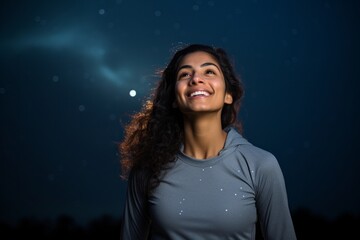 Poster - Portrait of a joyful indian woman in her 20s showing off a lightweight base layer isolated in sparkling night sky