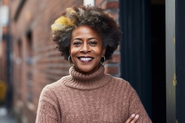 Poster - Portrait of a cheerful afro-american woman in her 60s wearing a cozy sweater while standing against vintage brick wall