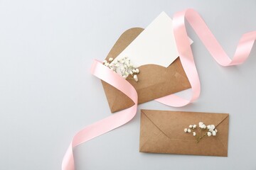 Poster - Blank card, envelopes, flowers and ribbon on light grey table, flat lay. Space for text