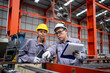 © KANGWANS - Two workers in a factory, one pointing at a clipboard. Scene is serious and focused