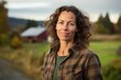 © Markus Schröder - Portrait of a grinning woman in her 40s dressed in a relaxed flannel shirt in front of quiet countryside landscape