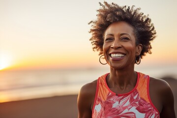 Wall Mural - Portrait of a happy afro-american woman in her 50s wearing a lightweight running vest while standing against beautiful beach sunset