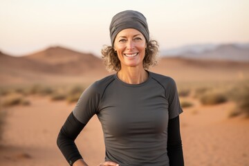 Canvas Print - Portrait of a grinning woman in her 50s showing off a lightweight base layer isolated in backdrop of desert dunes