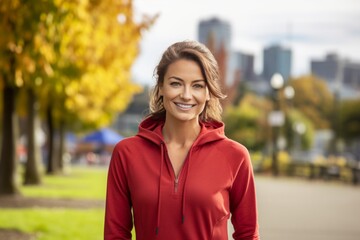 Poster - Portrait of a smiling woman in her 30s wearing a zip-up fleece hoodie in front of vibrant city park