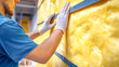 © Anoo - A worker installs yellow rock wool insulation in a metal frame wall for effective heat protection in a commercial construction project