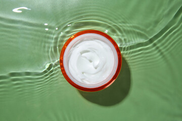 Poster - Jar with cream in water on light green background, top view. Cosmetic product