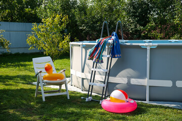 Poster - Above ground swimming pool, folding chair, towel, inflatable rings and ball in backyard