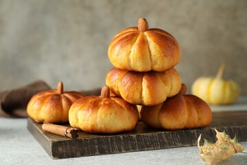 Wall Mural - Tasty pumpkin shaped buns and cinnamon on light grey table, closeup