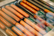 © Raivo - A close-up view of sausages cooking on a roller grill, showing shiny, cooked hot dogs ready to serve in a fast-food environment.