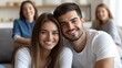 © Anna - A joyful couple poses for a picture while surrounded by friends in a casual, inviting living room filled with natural light. Laughter and smiles fill the air