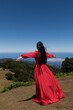 © Milou Dirks - rear view of woman in long red dress standing on a green mountain top in Fanal Forest overlooking the blue sea in Madeira, Portugal