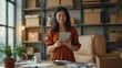 © natakot - A woman smiling as she reads something on her tablet in her cozy home office, surrounded by boxes and decor. The image reflects a cheerful, productive work-from-home setting.