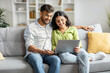 © Home-stock - Loving happy indian couple sitting on couch at home, embracing, using laptop computer, young man and woman watching movie online, copy space
