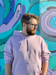 Millennial man in a pastel hoodie standing in front of a vibrant, abstract mural. Soft fabric and bold graffiti creates a striking contrast of modern urban style. Street urban style fashion