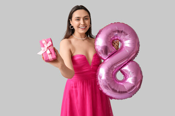 Sticker - Happy young woman with pink air balloon in shape of figure 8 and gift box on grey background. International Women's Day