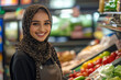 © wolfhound911 - A young adult Arabian female cashier beams with a friendly smile as she assists customers at her checkout station. The vibrant supermarket backdrop includes an array of fresh produce and goods,