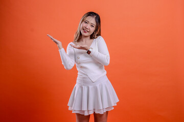 beautiful female gesture white top standing cheerful to camera both palms presenting to right isolated orange background. for fashion concept, advertising, promotion, commercial