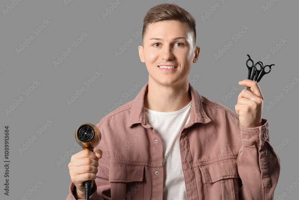 Male barber with hair dryer and scissors on grey background