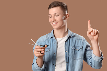 Wall Mural - Male barber with scissors pointing at something on brown background, closeup